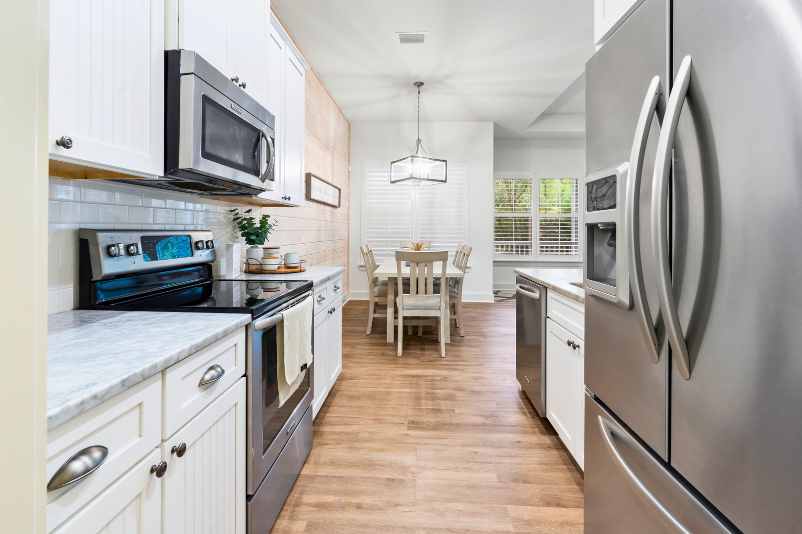 Bright coastal kitchen with stainless appliances, white cabinetry, warm wood floors, and an inviting open flow to dining.
