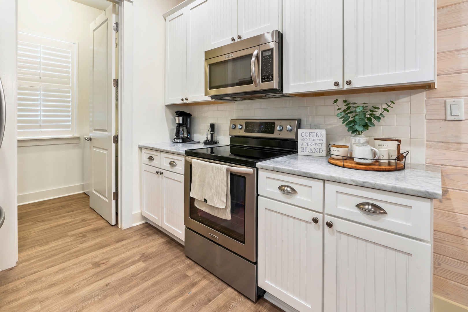 Fresh coastal kitchen with white shaker cabinets, stainless appliances, soft wood floors, and clean, beach-inspired style.