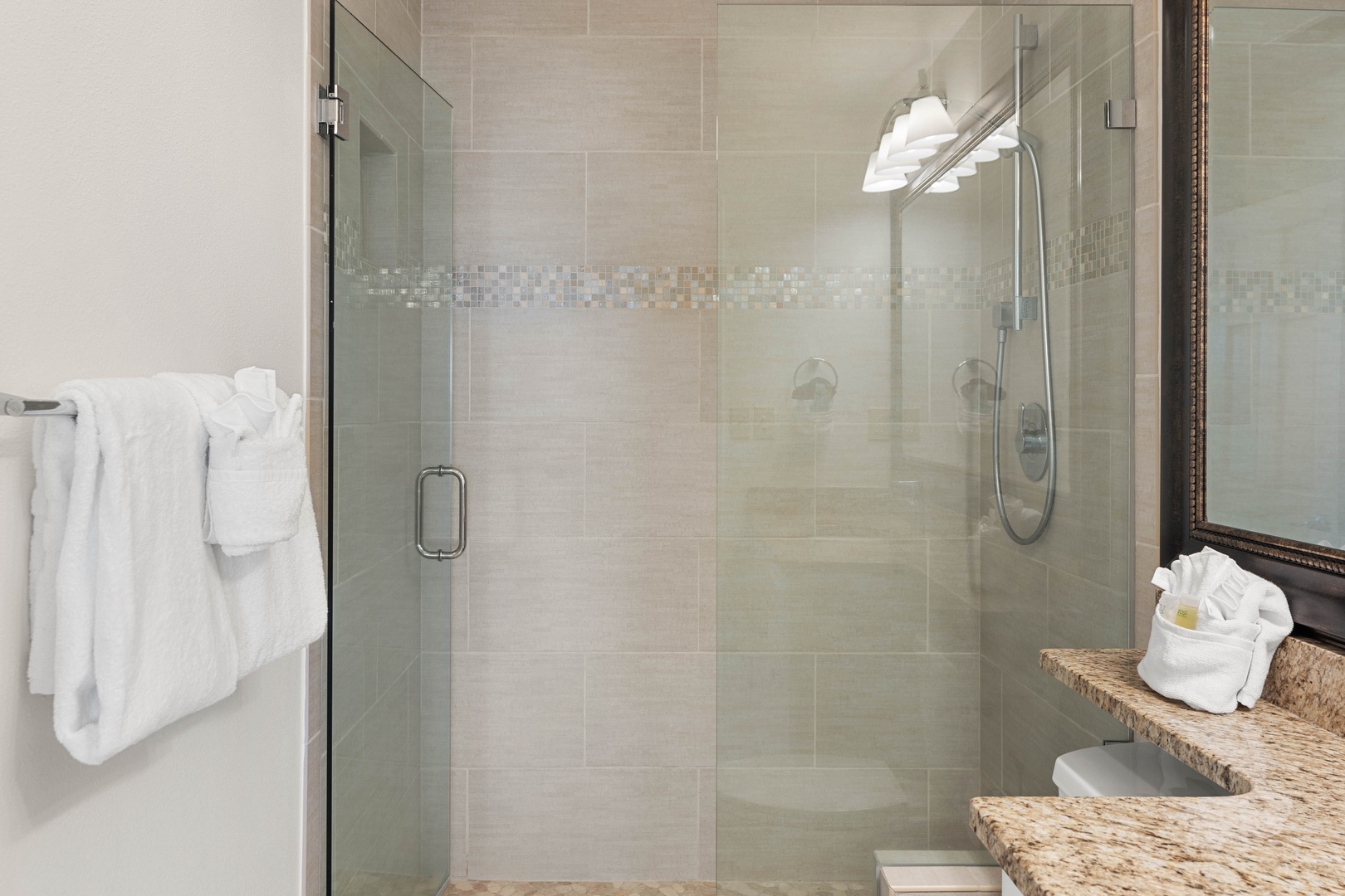 Step into your spa-like bathroom featuring a spacious glass shower with elegant mosaic tile details and plush towels ready for your stay.