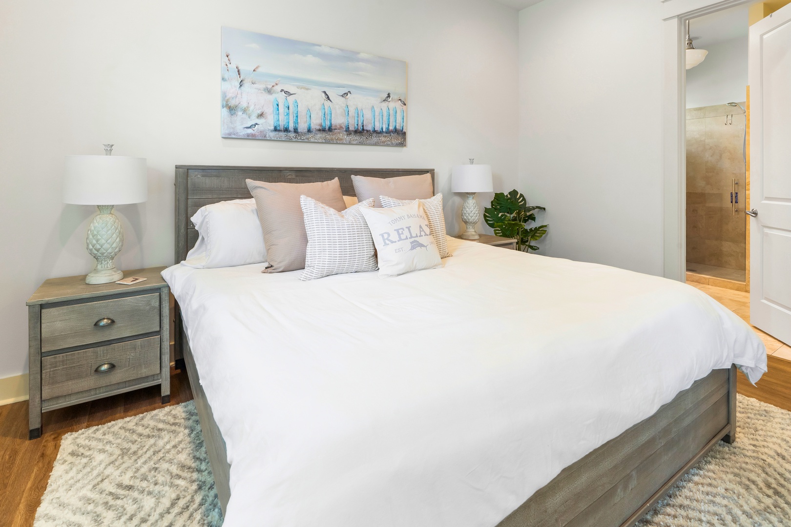 Sink into crisp white linens and coastal-inspired decor in your serene bedroom retreat, complete with stylish furnishings and soothing ocean artwork.