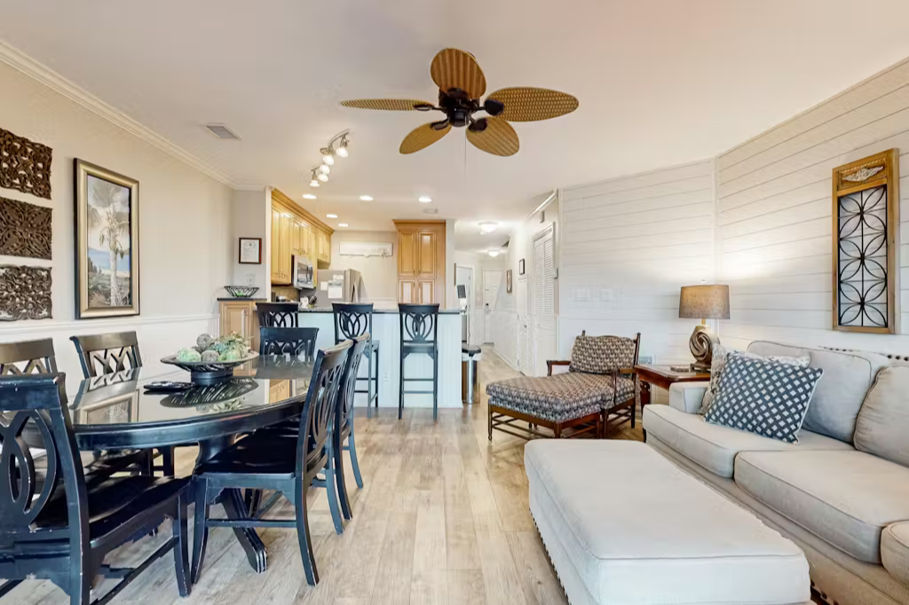Open-concept living space flowing seamlessly from living room to dining area and kitchen, featuring a plush sofa, elegant dining table, and coastal charm with warm, inviting décor.