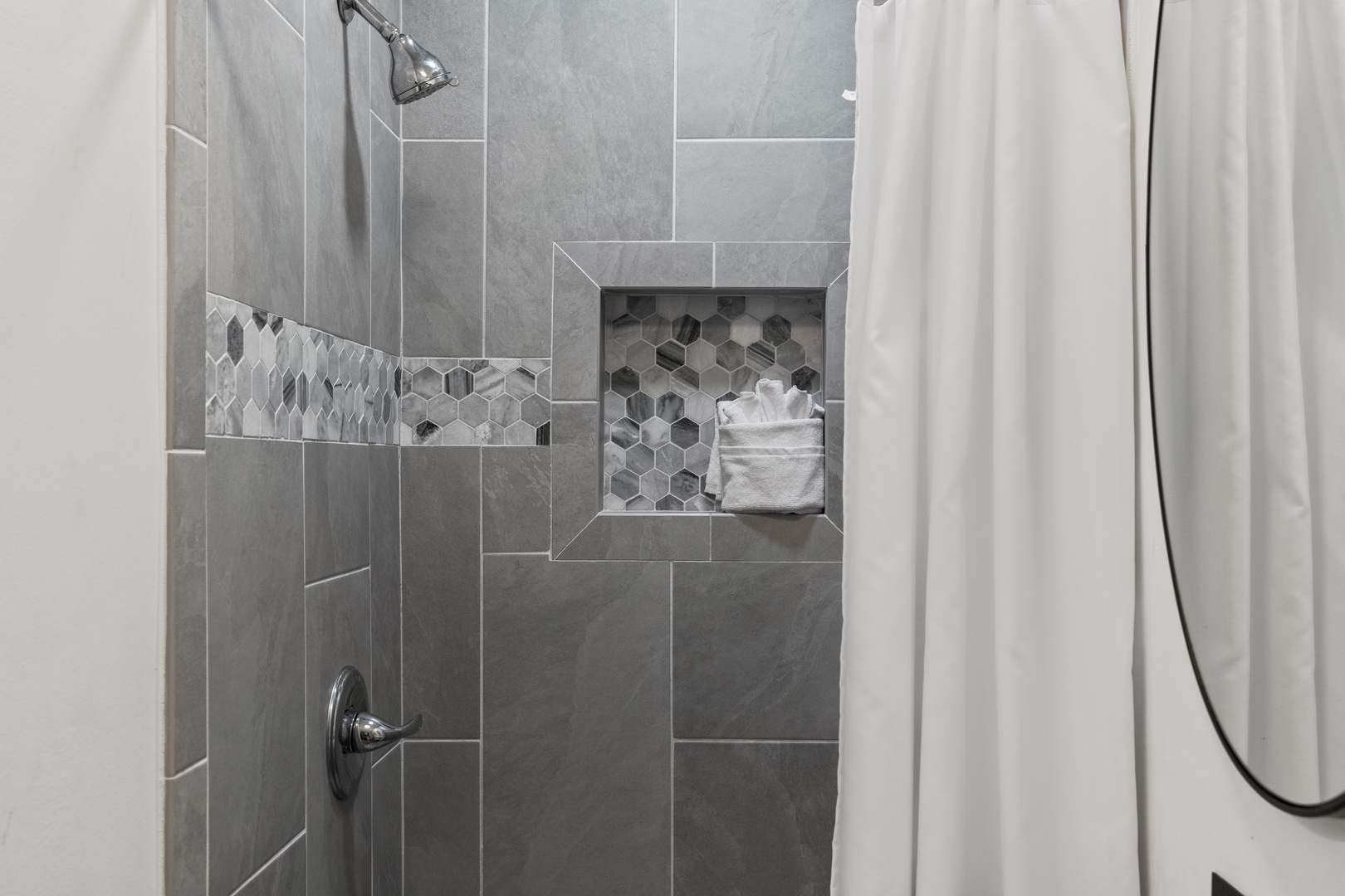 Step into your sleek tiled shower featuring modern gray tiles, hexagon accent details, and a convenient built-in niche for your toiletries.