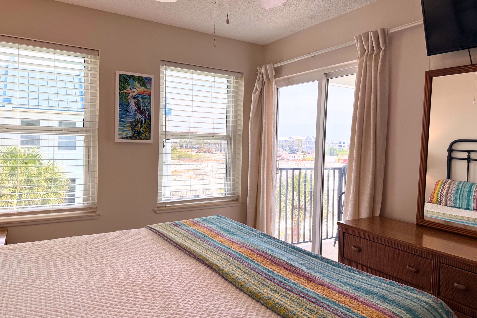 Bright, beachy primary bedroom featuring colorful tropical artwork and stunning water views from your private balcony. Relax in comfort with thoughtful furnishings and natural light.