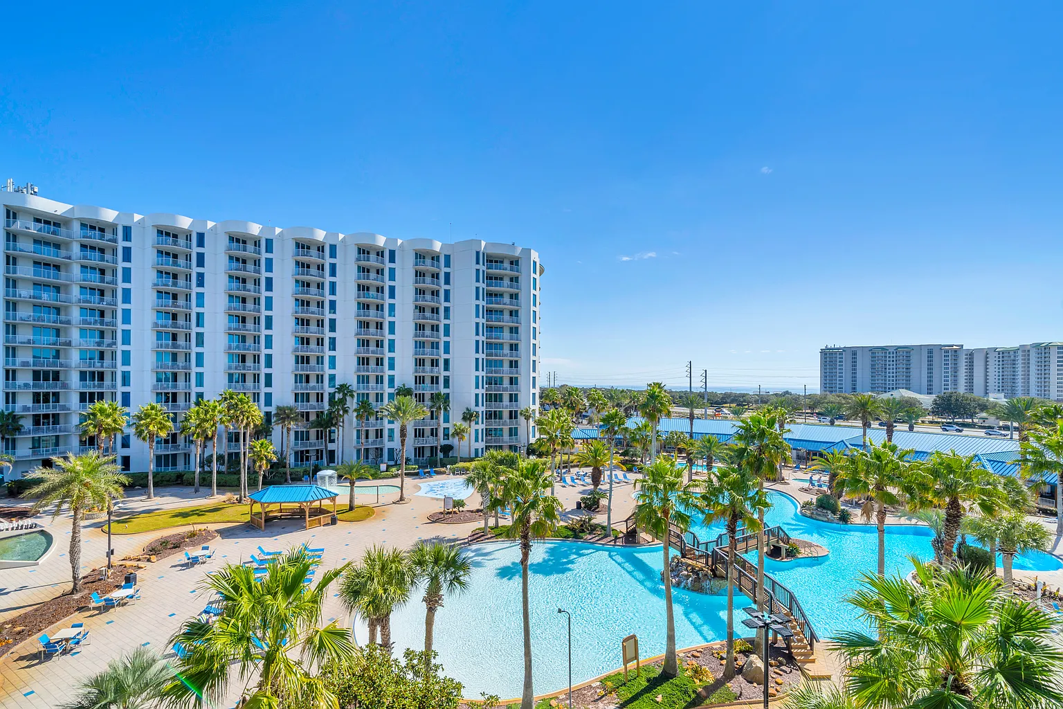 Modern beachfront resort with expansive pool complex featuring water slides and tropical landscaping under clear blue skies.