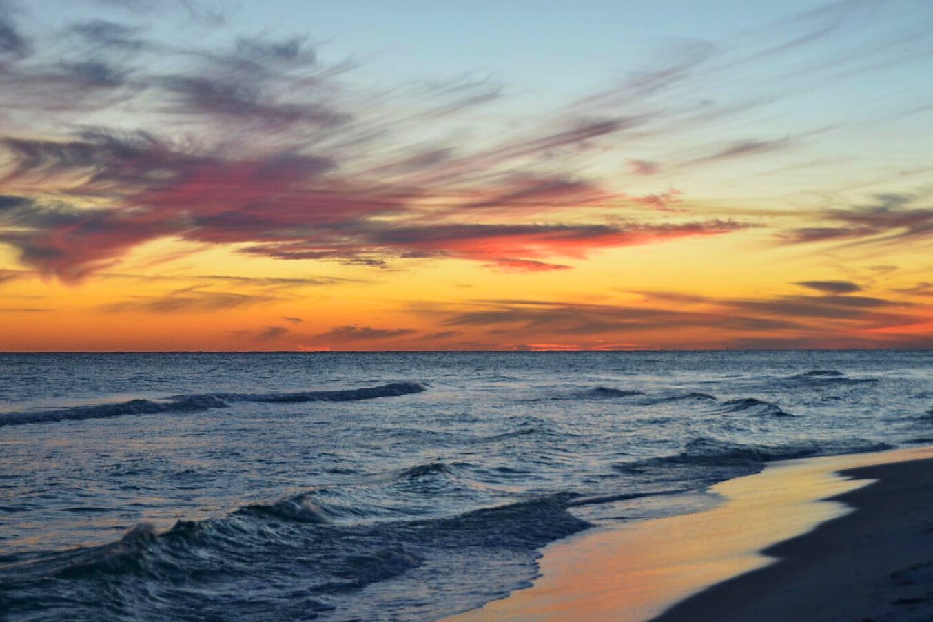 Golden-hour Gulf sunset with vibrant streaks of color across the sky, gentle waves rolling ashore, and a peaceful shoreline that invites reflection, relaxation, and evening beach walks.