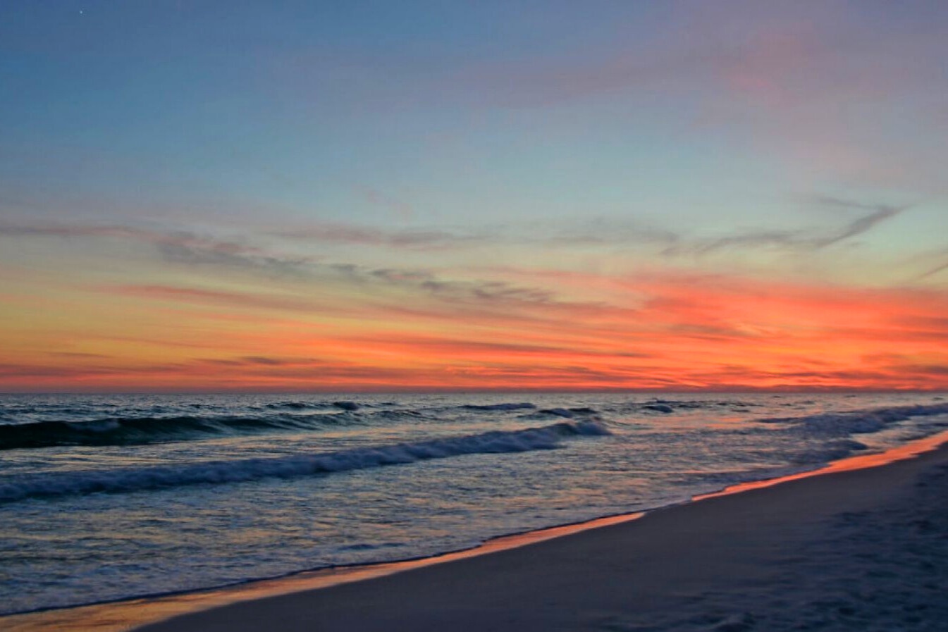 Stunning Gulf sunset with colorful skies reflecting over gentle waves and sugar-white sand, creating a serene coastal scene perfect for evening strolls and quiet moments by the water.