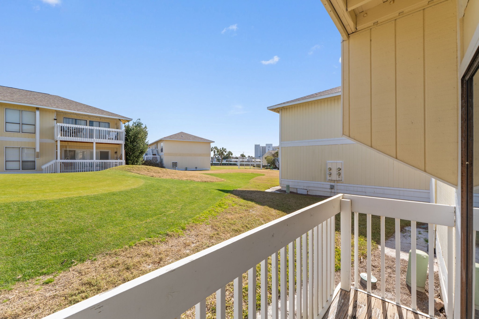 A peaceful residential property with neighboring buildings, open green space, and distant city skyline visible from the balcony.