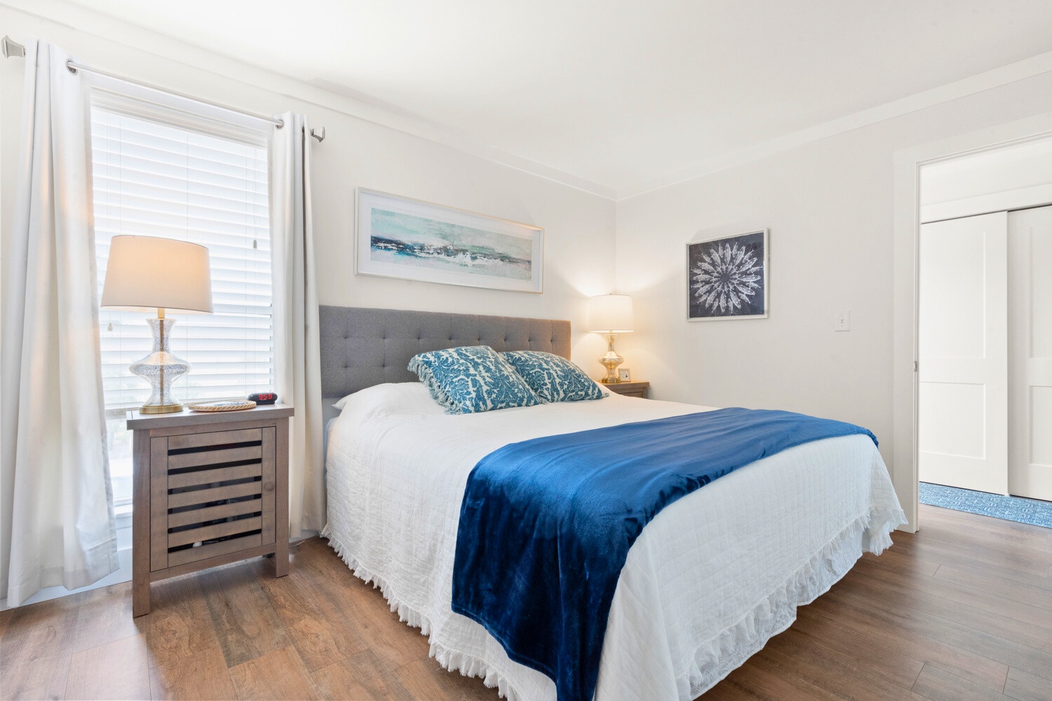 Sink into crisp white linens and ocean-inspired blue accents in your peaceful bedroom retreat, where coastal artwork creates a serene escape.