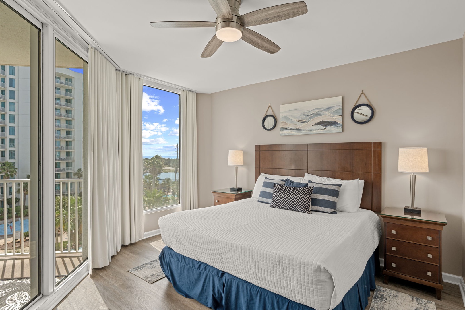 Unwind in your coastal-inspired bedroom with soft linens, nautical touches, and a ceiling fan to keep you cool—wake to peaceful views of palms and poolside relaxation right beyond your balcony.
