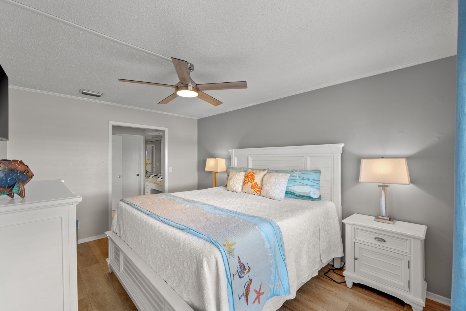 The primary bedroom offers a comfortable king bed, coastal-inspired décor, and a peaceful atmosphere perfect for relaxing after a day at the beach. A bright and inviting retreat designed for comfort and rest.