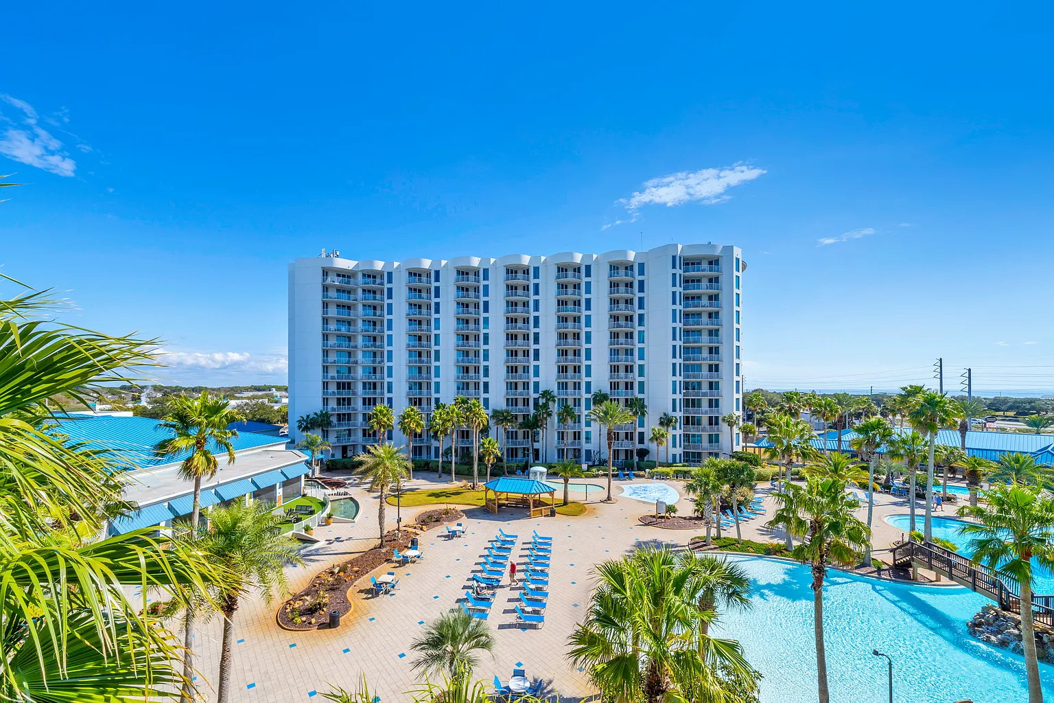Modern white resort tower rises above tropical palms and sparkling pools in this coastal paradise setting.