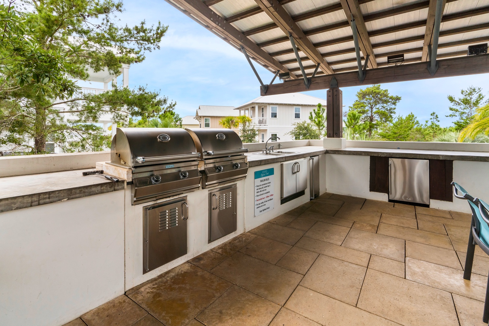 Outdoor coastal kitchen with built-in grill, bar seating, stainless appliances, and relaxed resort-style vibes.