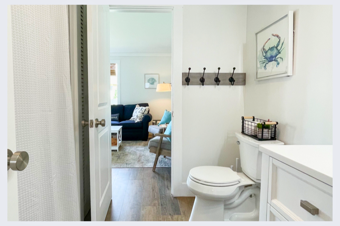 Your private powder room features coastal charm with thoughtful hooks and storage, connecting seamlessly to the bright living space.