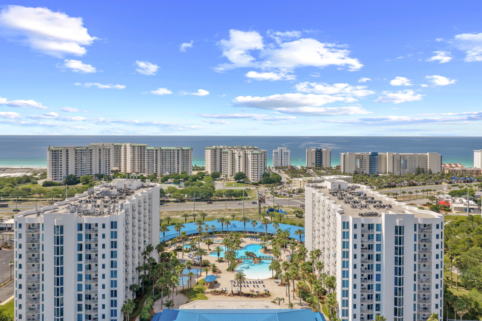 Aerial view of the beachfront property showcasing the spacious pool area, palm-lined grounds, and the stunning emerald waters of the Gulf Coast in the distance.