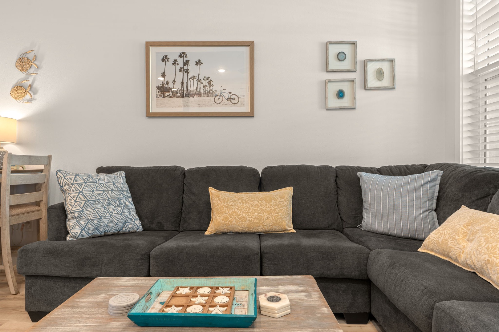 Unwind on your plush sectional sofa with coastal decor and thoughtful touches like a tic-tac-toe game, perfect for family fun and relaxation in your beach-inspired living space.