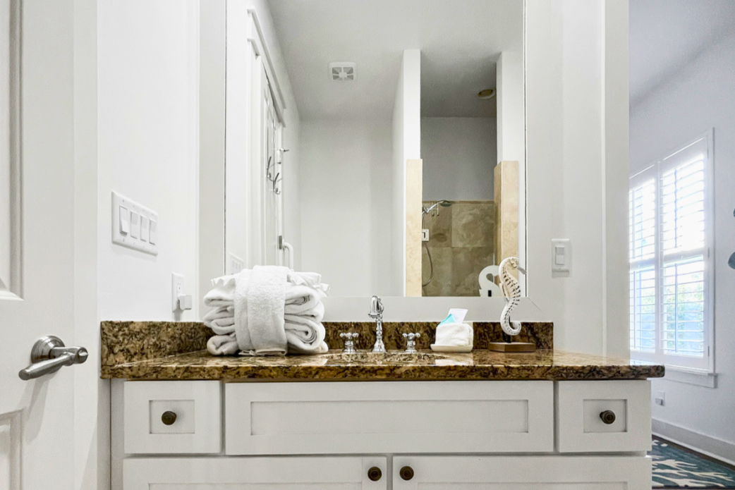 Fresh coastal bathroom with a wide granite vanity, white cabinetry, soft lighting, and a clean, beach-relaxed feel.