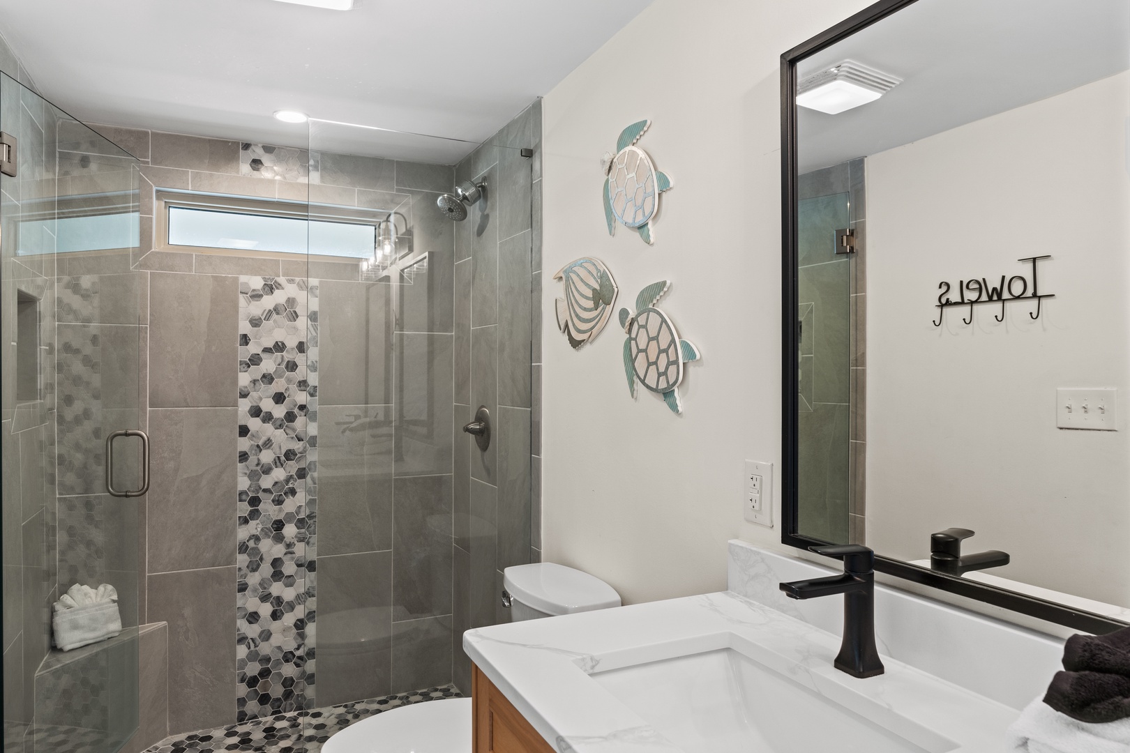 Step into your spa-like bathroom where the mosaic-tiled walk-in shower and coastal turtle artwork create a serene retreat.
