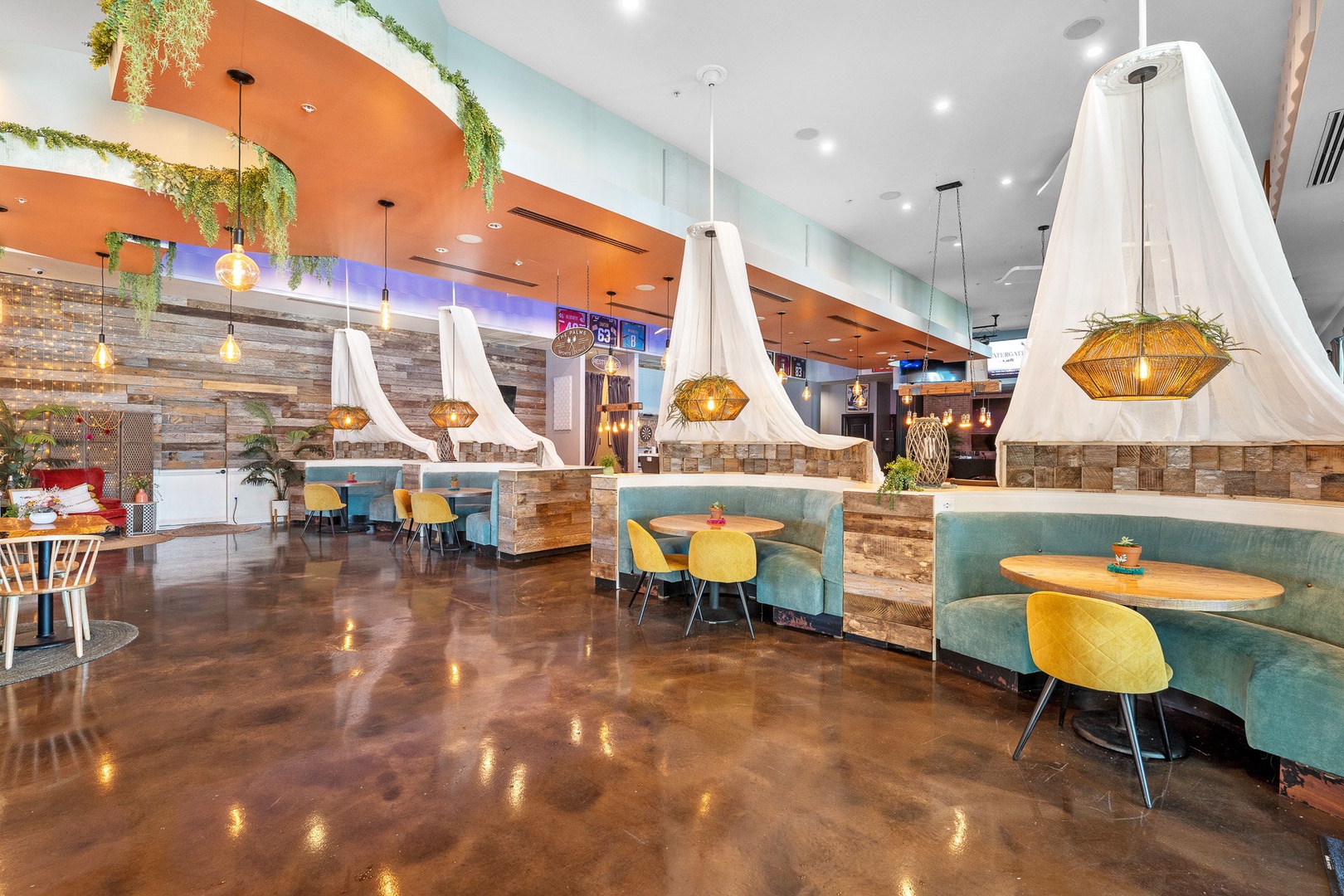 A vibrant communal dining area featuring stylish booth seating, unique lighting, and tropical greenery creating an inviting space where you can enjoy meals and socialize with fellow travelers.