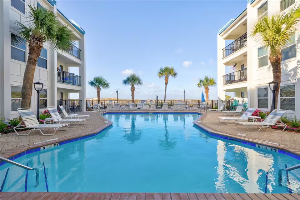 Resort-style beachfront pool surrounded by palms and loungers—relax and soak in the coastal views just steps from the beach.