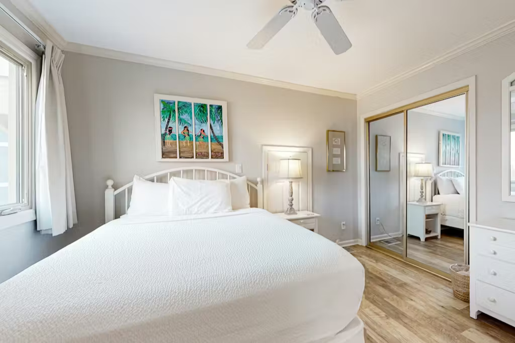 Sink into the plush white bedding and unwind in your serene retreat. The soft neutral tones, warm wood floors, and gentle ceiling fan create a peaceful ambiance perfect for restful nights.