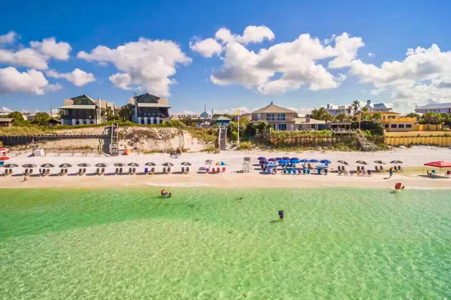 Crystal clear waters meet pristine white sand at this stunning beachfront location with colorful umbrellas and vacation homes.