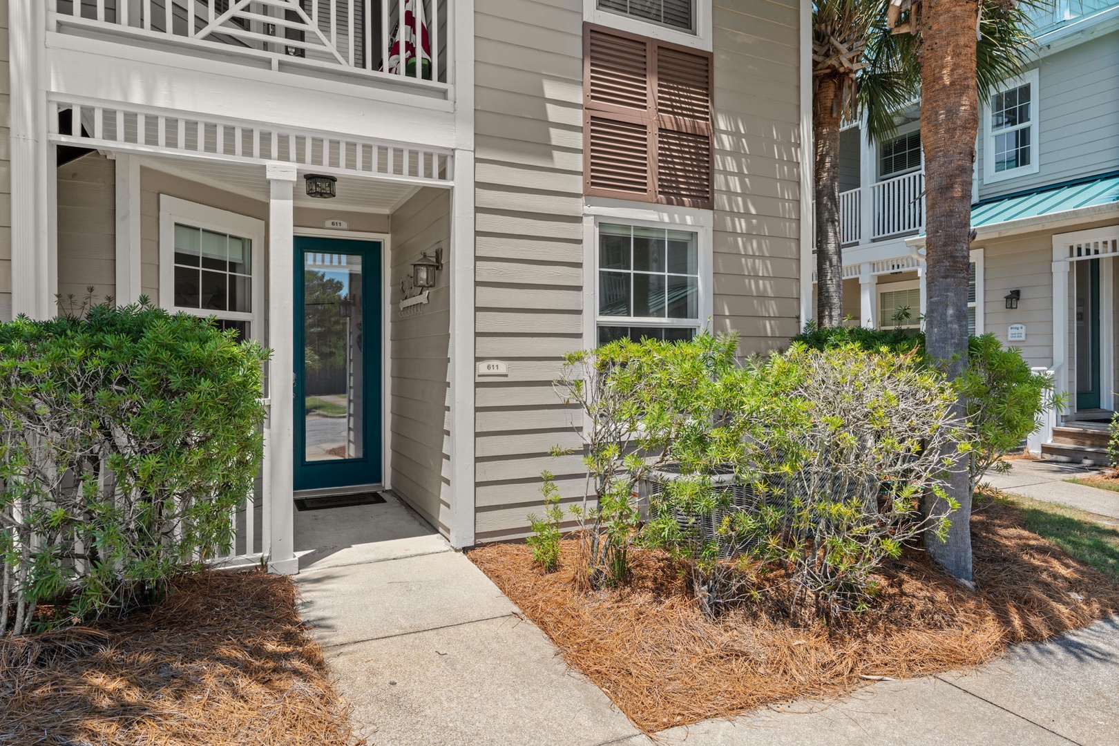 Welcoming coastal property entrance surrounded by lush landscaping and swaying palm trees, creating a peaceful arrival experience in this charming residential neighborhood.