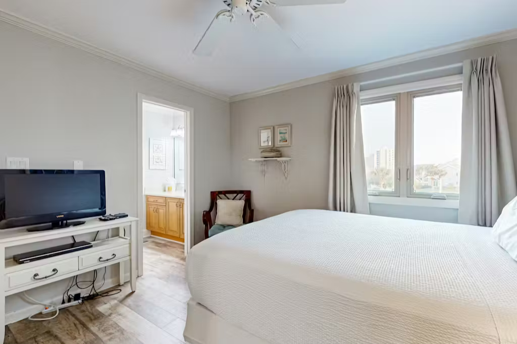 Cozy bedroom with soft natural light, a comfortable bed, TV, and charming sitting area, plus easy access to the adjacent bath.
