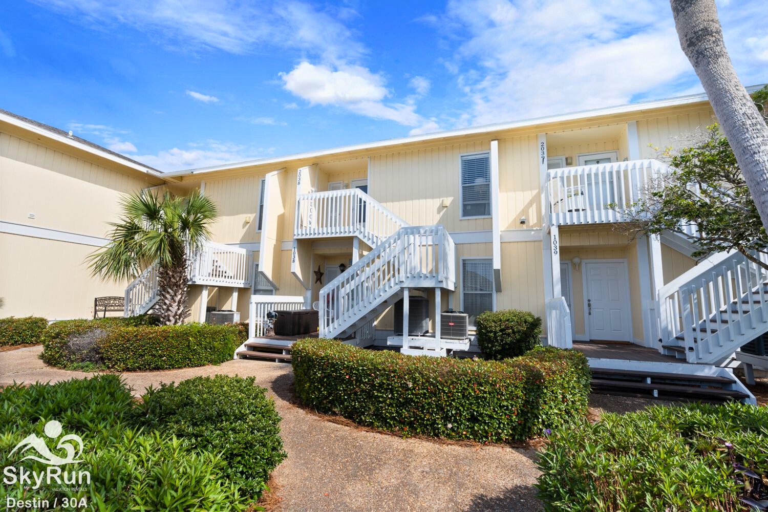 Bright coastal complex with tropical landscaping and multiple balconies under a stunning blue sky.