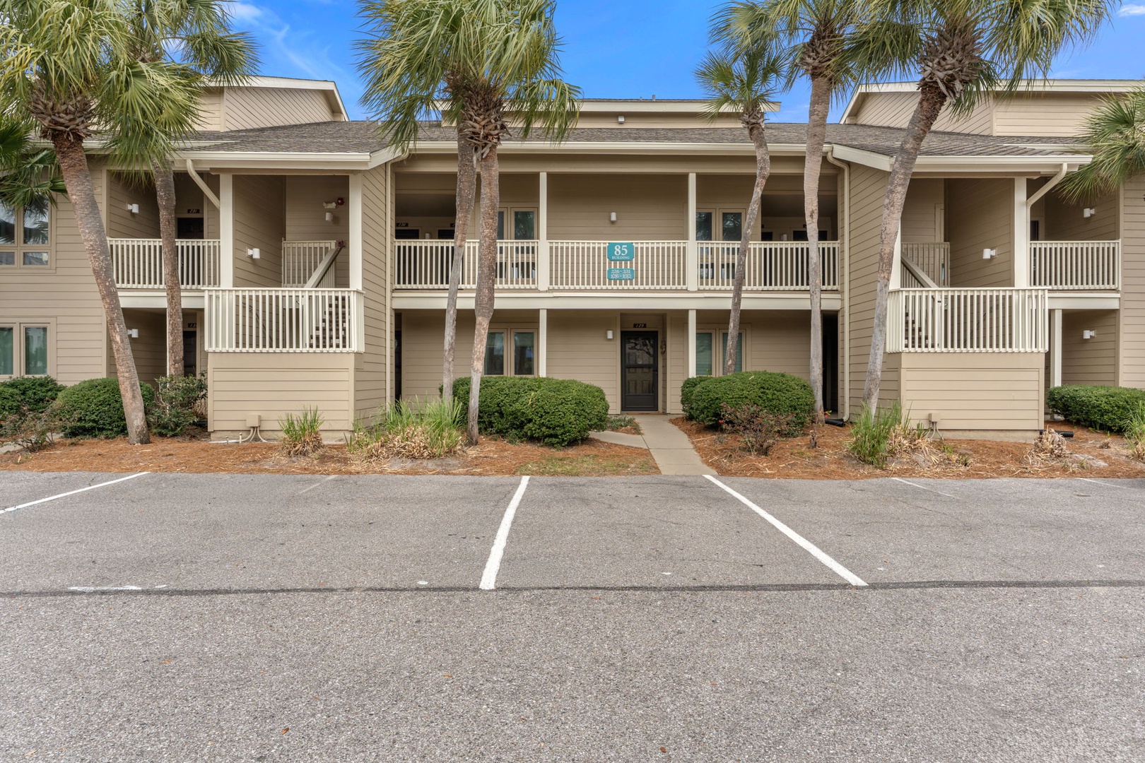 A welcoming two-story property surrounded by tropical palm trees with dedicated parking spaces and well-maintained landscaping.