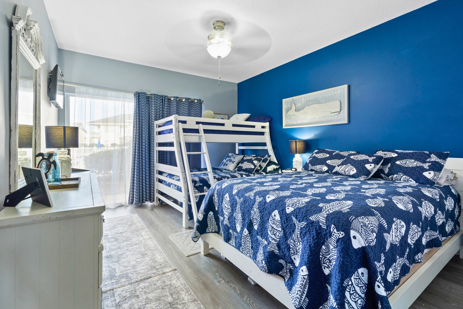 Unwind in this vibrant blue bedroom featuring comfortable bunk beds and a queen bed, perfect for families seeking coastal-themed comfort.