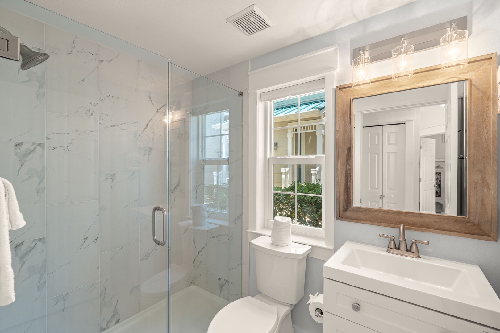 Step into your beautifully updated bathroom featuring elegant marble-style tile, a spacious walk-in shower, and a charming natural wood-framed mirror that brings warmth to your morning routine.