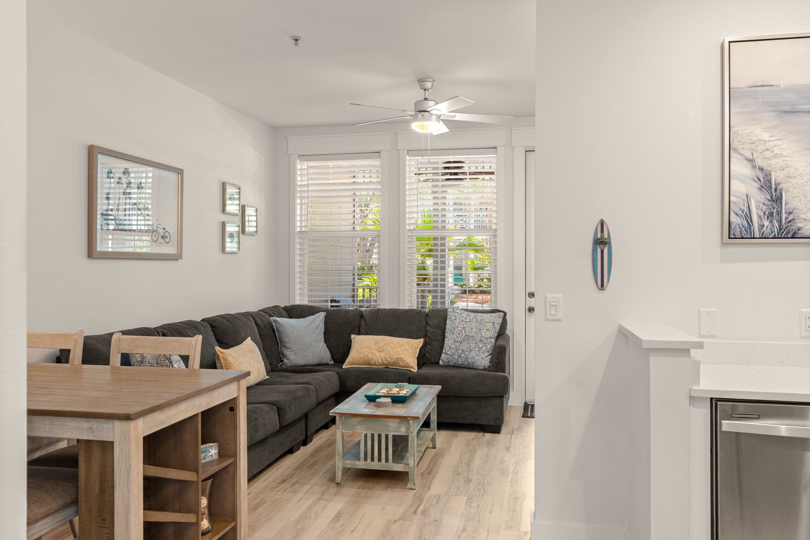 Step into your bright, airy living space where coastal charm meets modern comfort. Unwind on the plush sectional, feel the gentle breeze from the ceiling fan, and let natural light pour through plantation shutters.