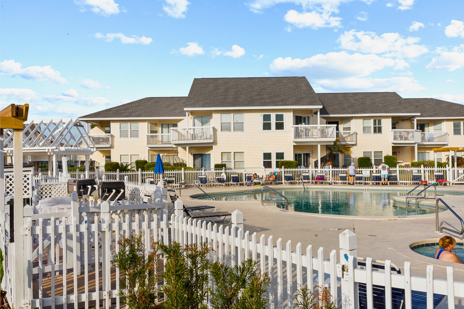 Multi-story vacation rental complex featuring private balconies overlooking a sparkling community pool with hot tub and outdoor seating areas.