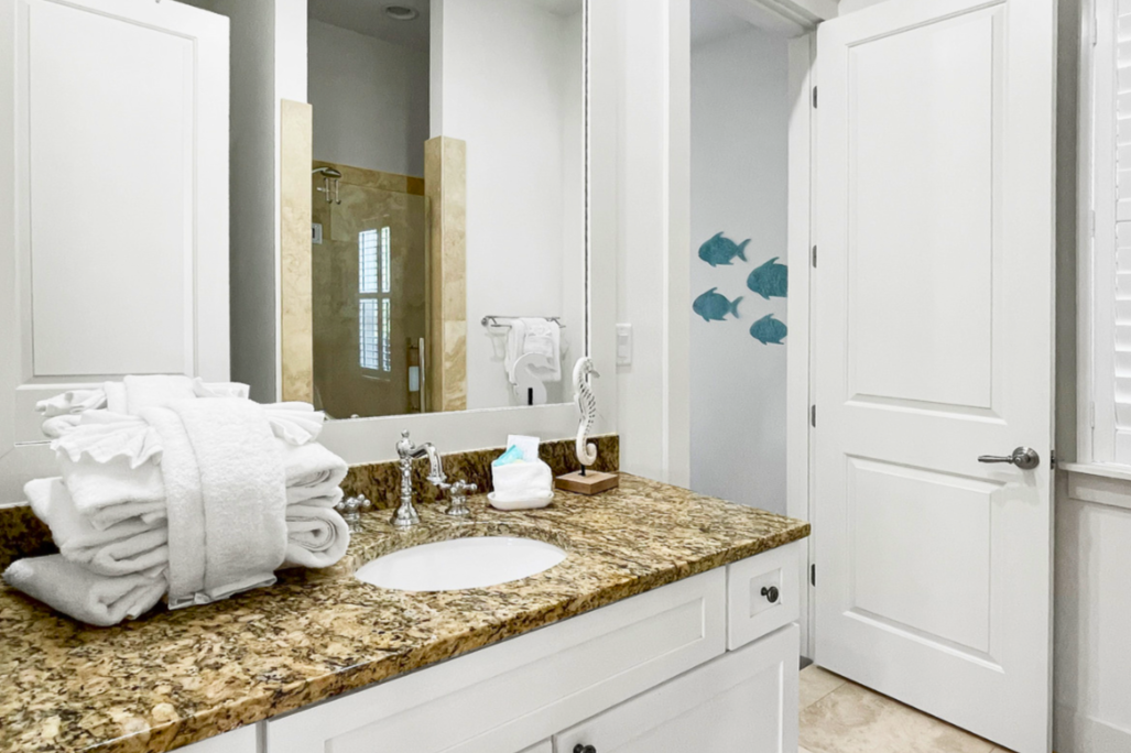 Bright coastal bathroom with granite vanity, crisp white cabinetry, nautical accents, and a fresh, spa-like feel.
