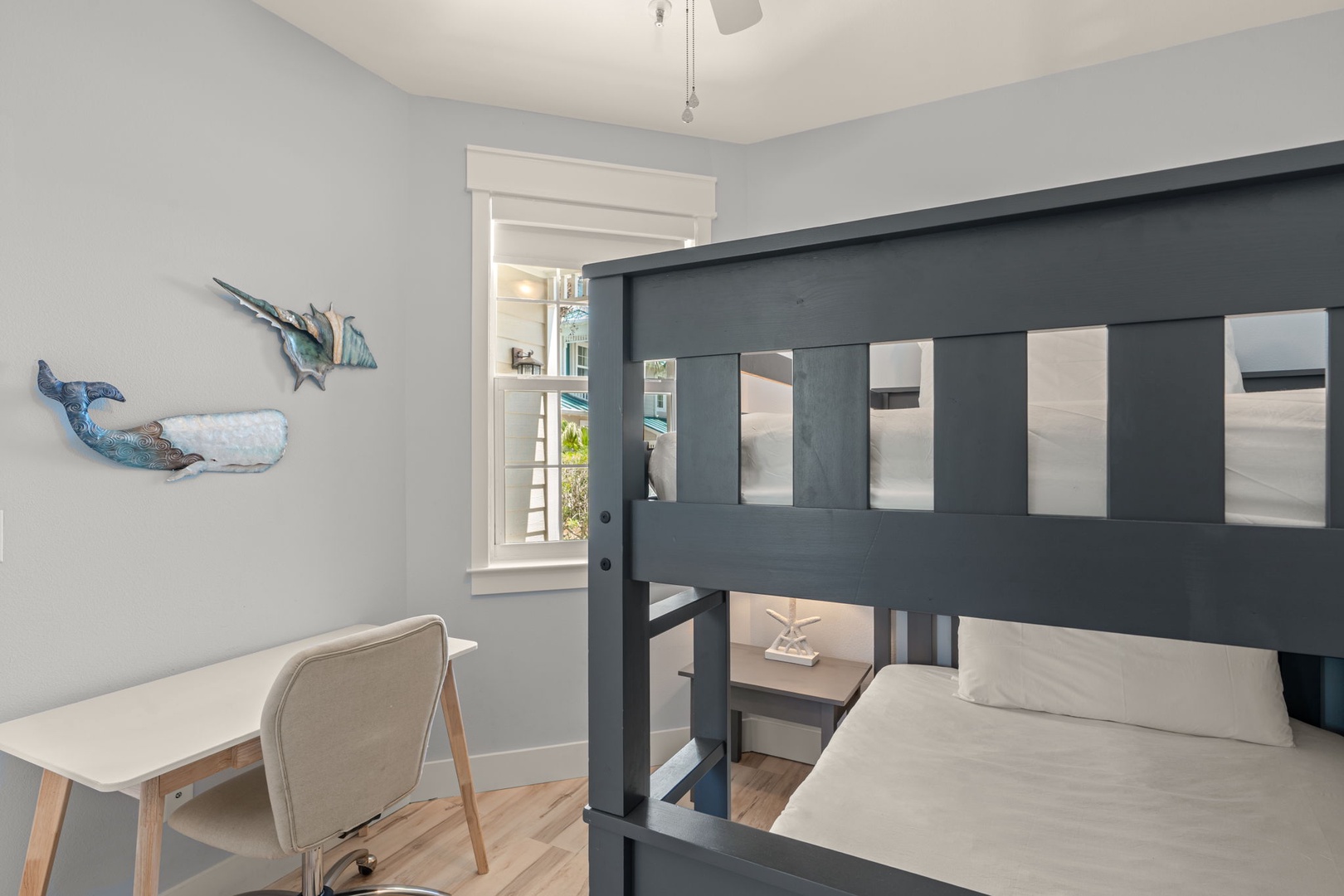 Your kids will love this charming coastal bedroom featuring a fun bunk bed setup and a dedicated workspace. Playful whale artwork adds whimsical touches to the serene blue-gray walls.