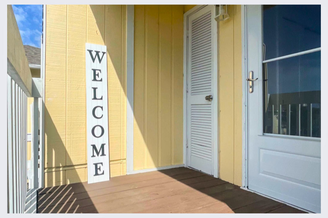 Bright yellow building entrance with welcoming white door and covered porch area for guest arrivals.