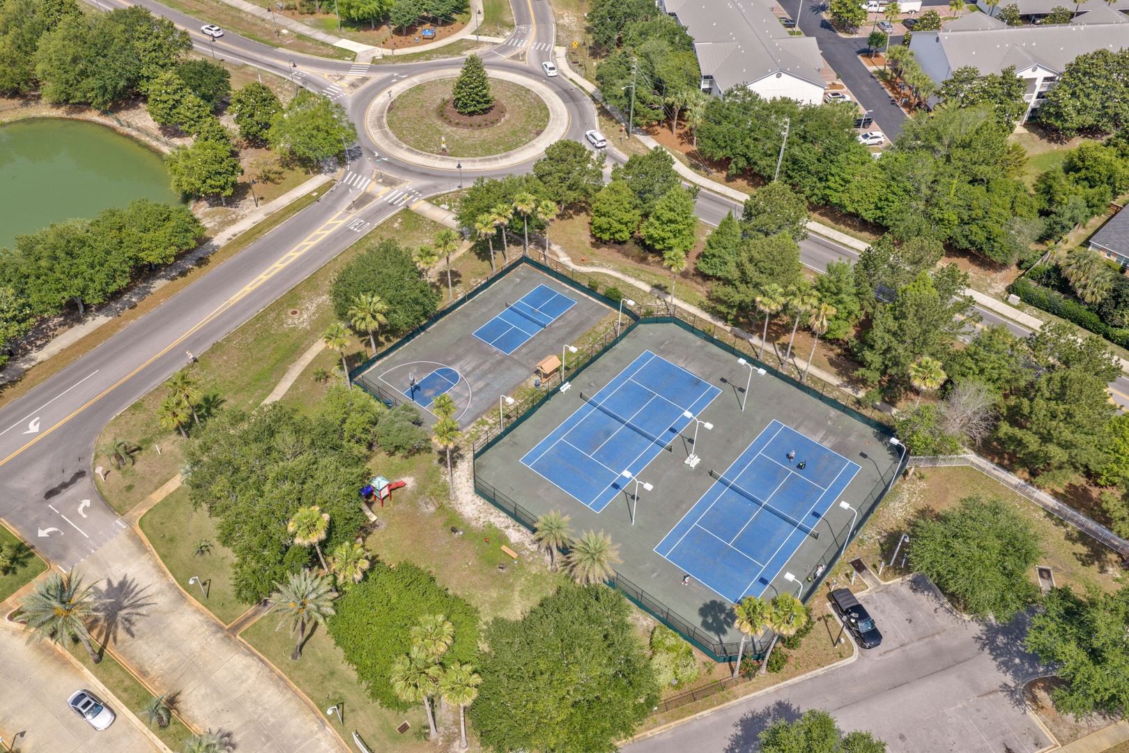 Aerial view of the community tennis courts located near a landscaped roundabout, surrounded by mature trees and residential streets, offering convenient access for property guests.