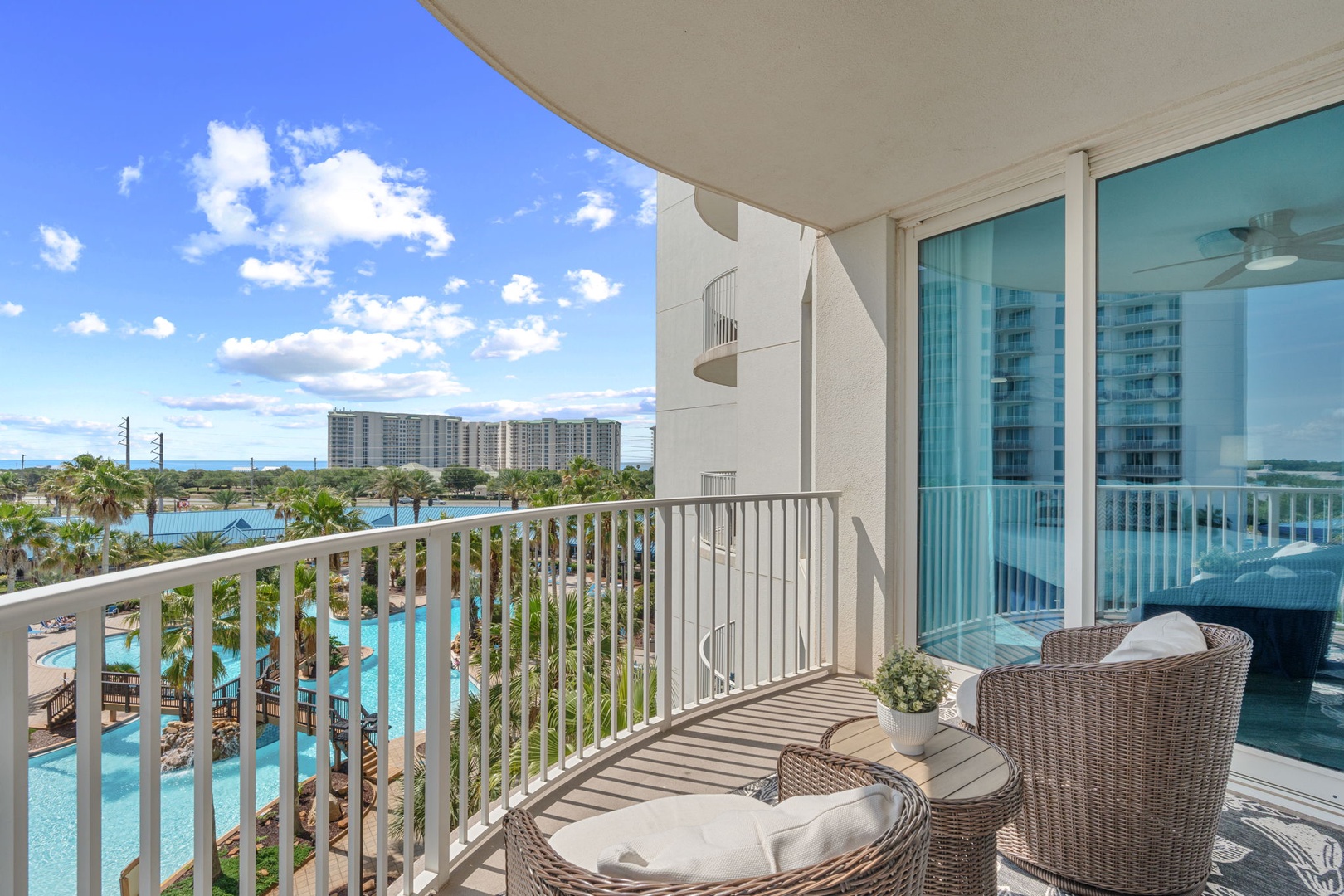 Balcony overlooking resort pools, palm trees, and distant beachfront high-rises under a clear blue sky—an ideal setting for arrival and exploring the surrounding area.