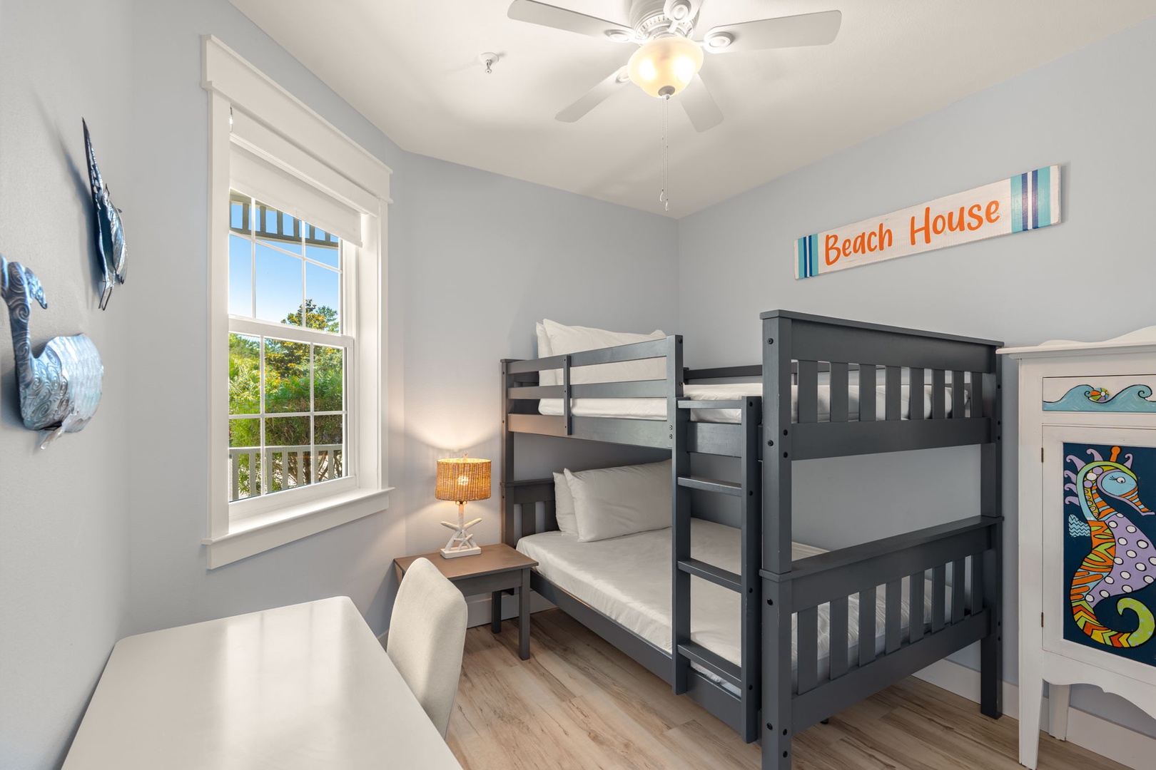 This cheerful room features a charming bunk bed perfect for kids, with beach-inspired decor and natural light streaming through the window to set a relaxed, coastal vibe.