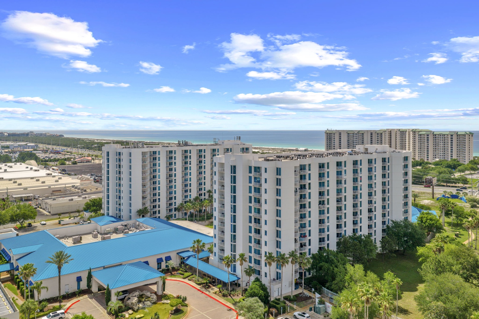 A beachfront resort property surrounded by palm trees and lush landscaping, with the Gulf of Mexico and sandy shoreline visible in the background.