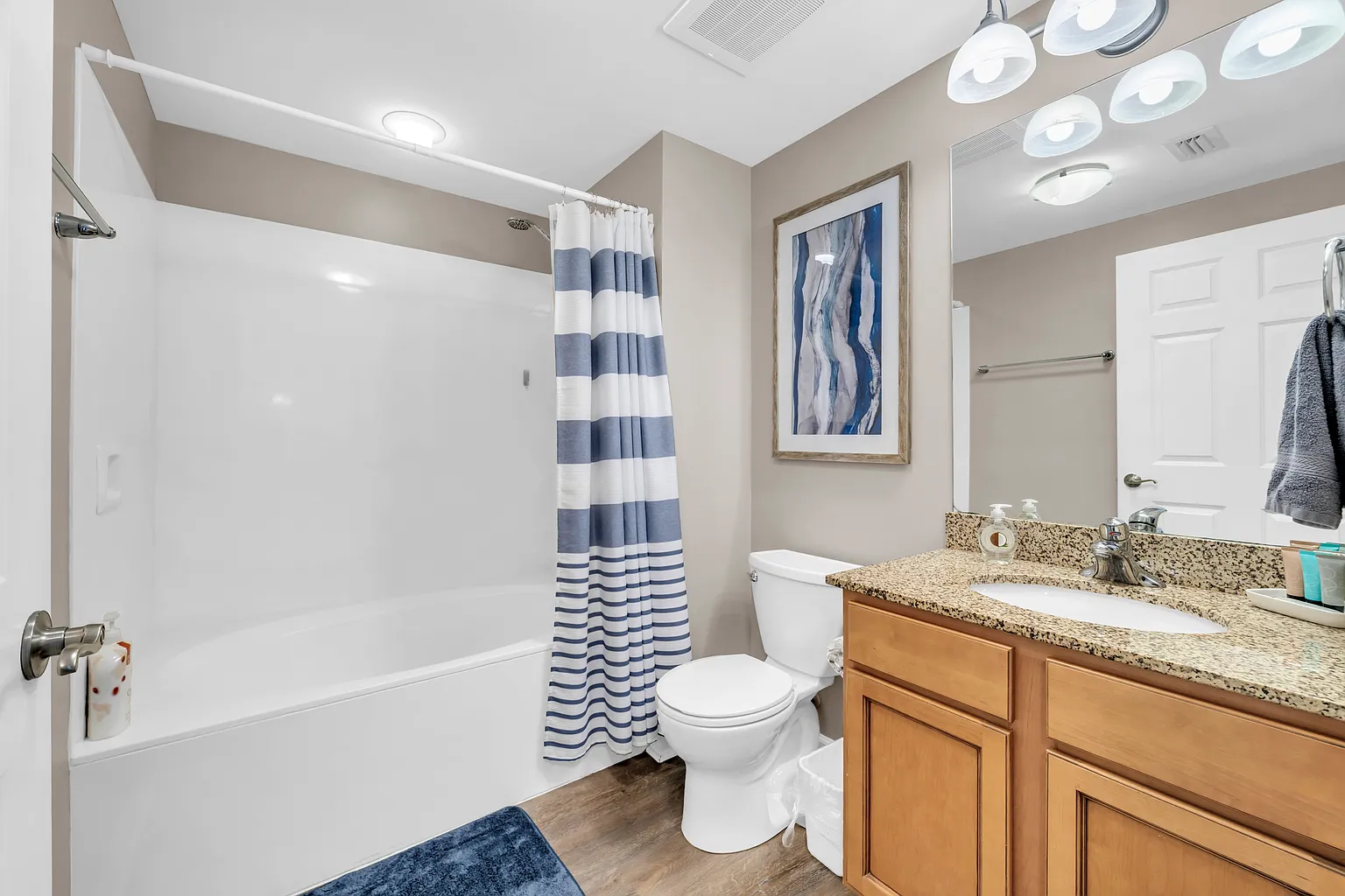 Refresh in your stylish bathroom with granite countertops, spacious tub-shower combo, and coastal-inspired blue striped curtain.