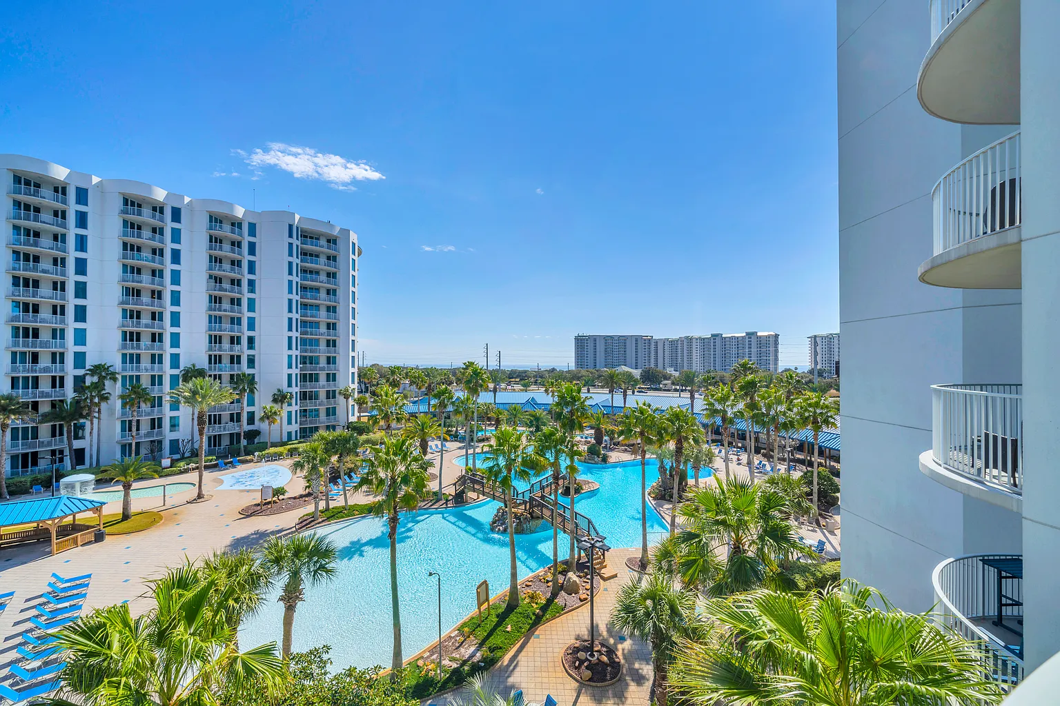 Expansive resort complex featuring multiple swimming pools, waterfront views, and modern high-rise buildings under clear blue skies.