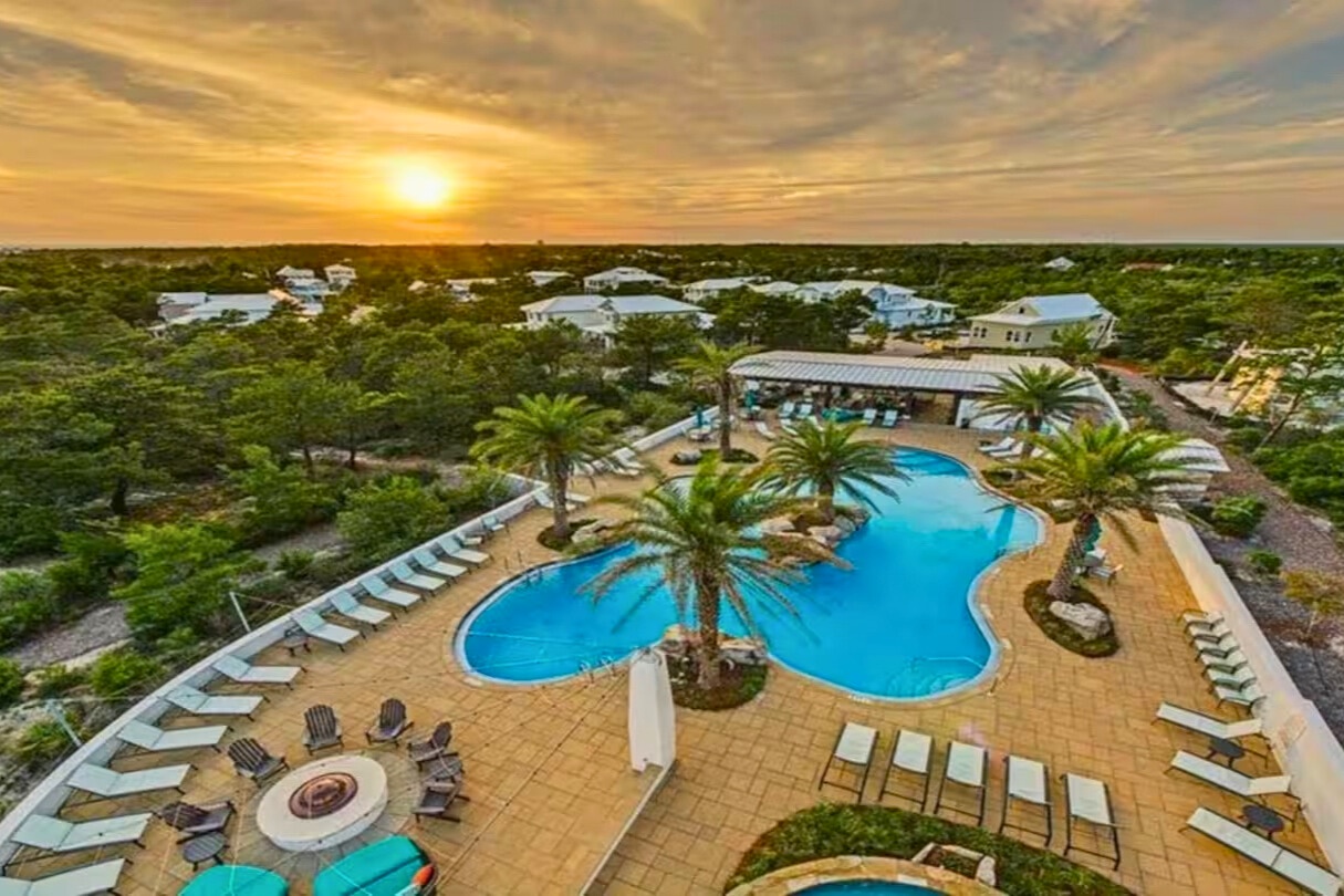 Stunning aerial view reveals the community's curved swimming pools, palm trees, and fire pit at golden hour.