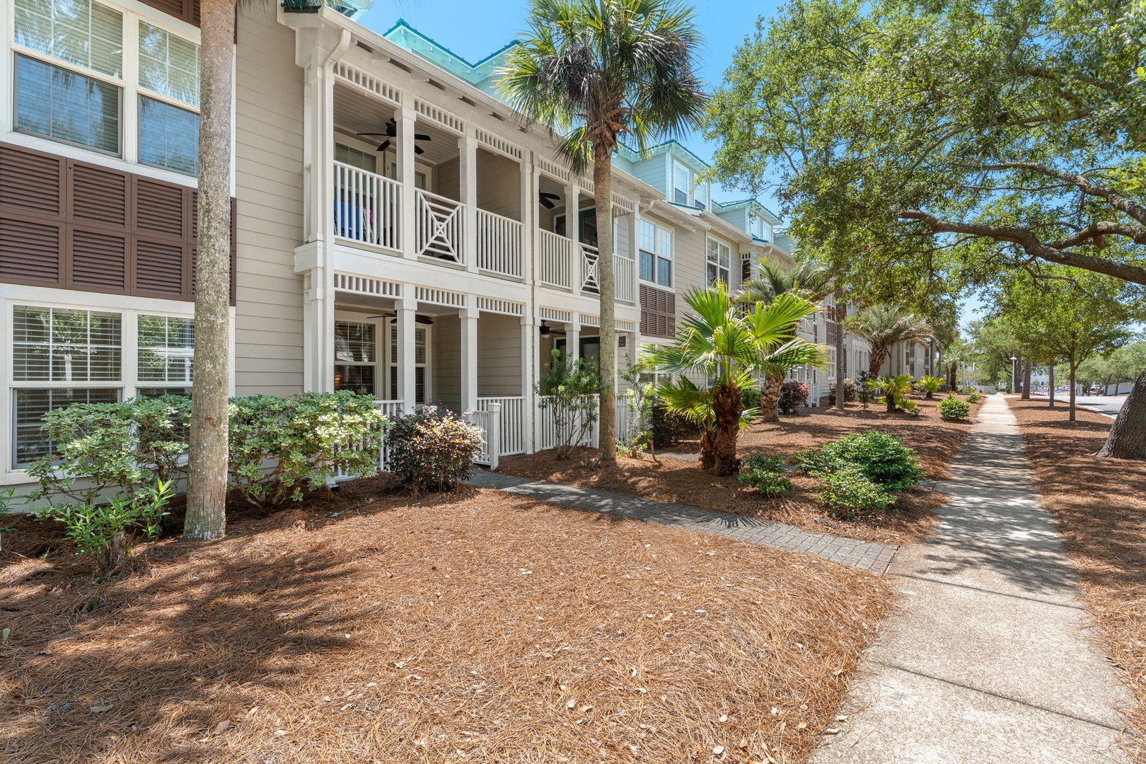 Charming coastal architecture with classic double-decker porches and lush landscaping along a quiet, tree-shaded walkway perfect for peaceful strolls.