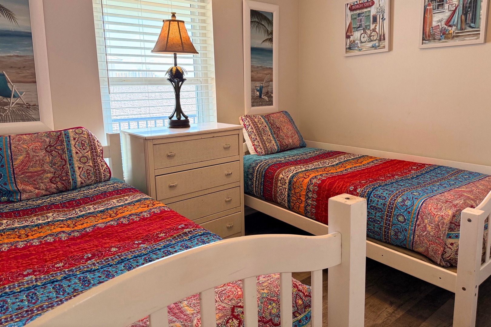 Unwind in your coastal-inspired guest bedroom featuring two twin beds with vibrant bohemian quilts, a charming bedside lamp, and beachy artwork that'll transport you to paradise.