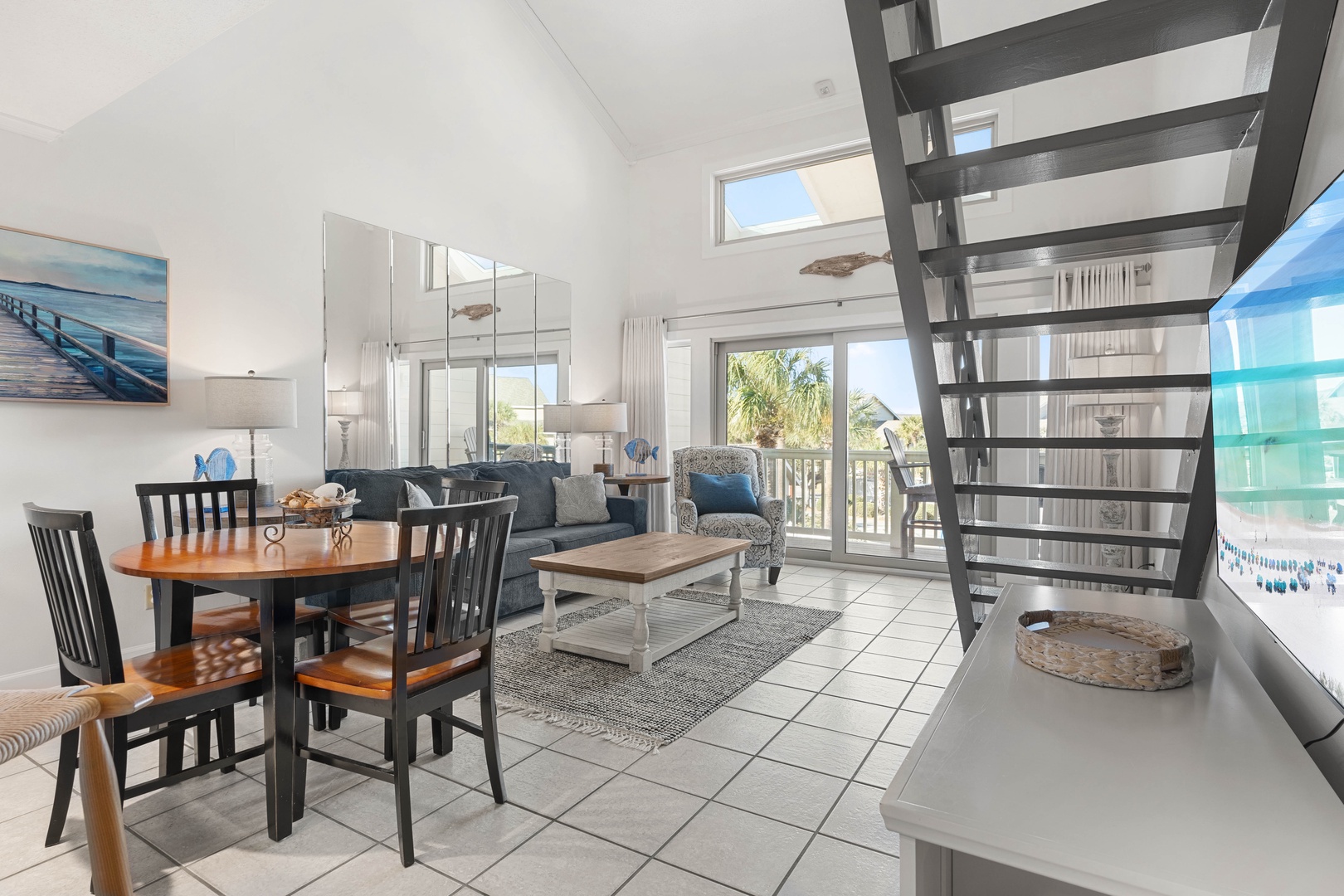 Your bright coastal retreat features an open-plan living space with ocean-inspired decor, comfortable seating, and large windows flooding the room with natural light.