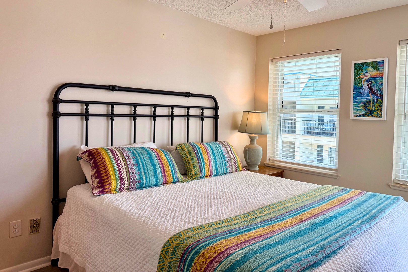 Your primary bedroom retreat features a comfy bed dressed in vibrant linens, soft natural light, and cheerful coastal artwork to start your mornings peacefully.