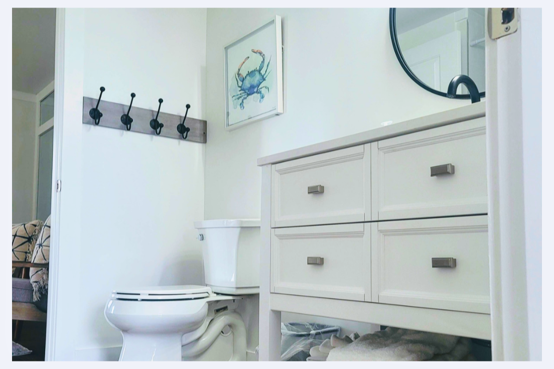 Your bright bathroom features coastal charm with a vanity offering ample storage and convenient wall hooks for your belongings.
