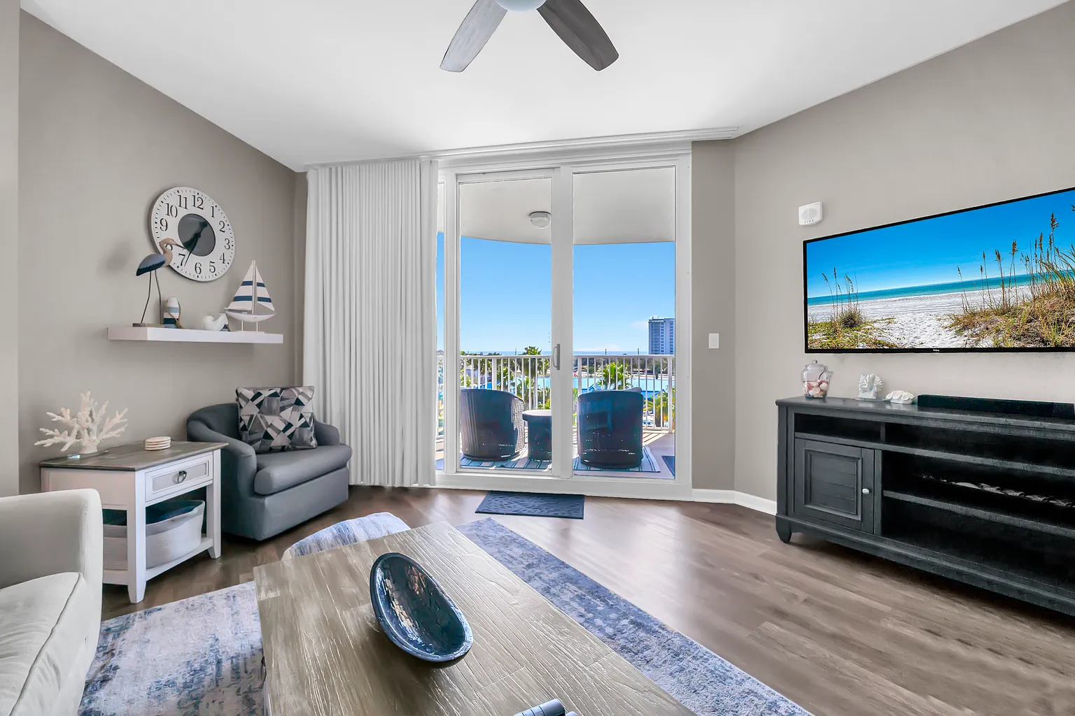 Relax in your coastal-themed living room with stunning balcony views and modern entertainment center.