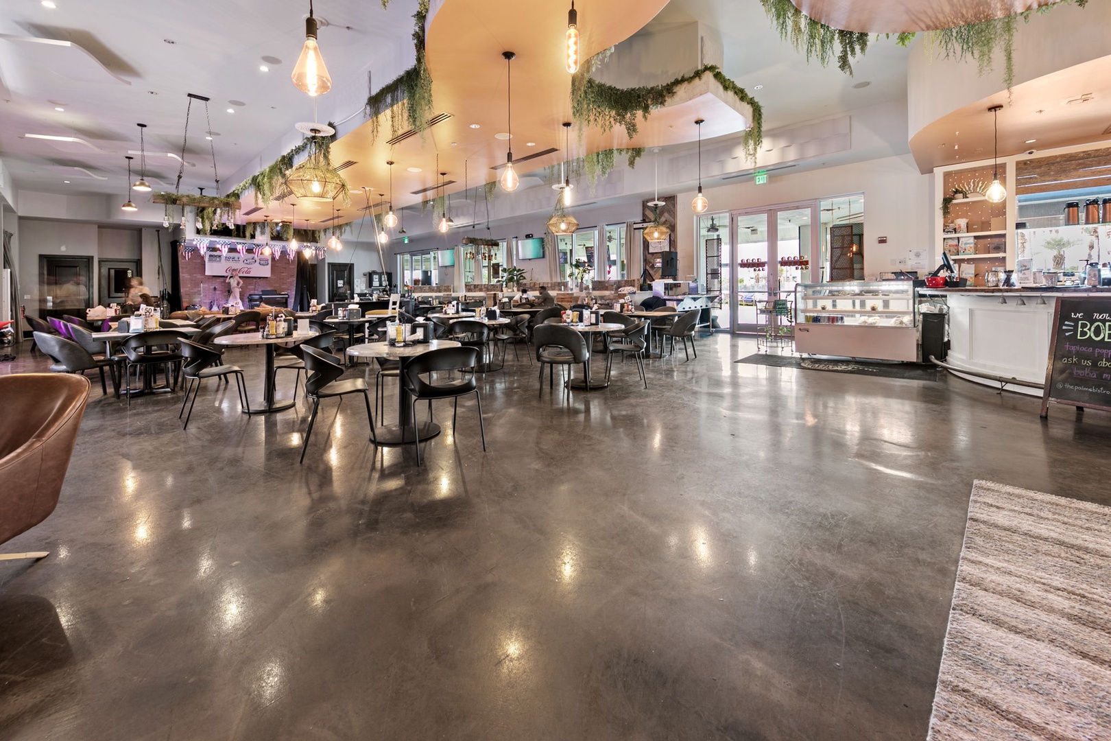 Stylish communal dining space with modern décor, hanging greenery, warm lighting, and a welcoming café corner—perfect for unwinding or connecting with fellow travelers.